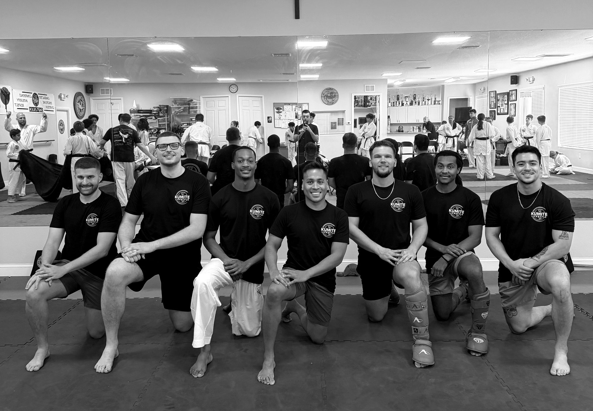 Seven of the Kumite team in Kumite tees, kneeling on the mat at a karate dojo
